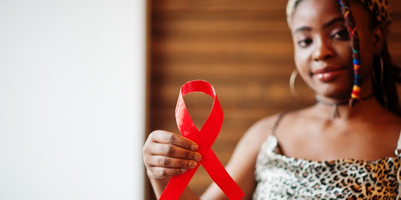 An individual holding a red HIV awarness ribbon.