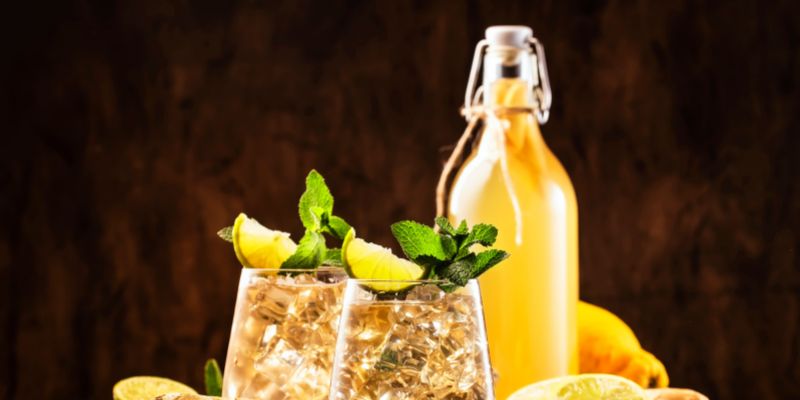 Two garnished glasses of ginger ale with a full bottle of ginger ale next to it.