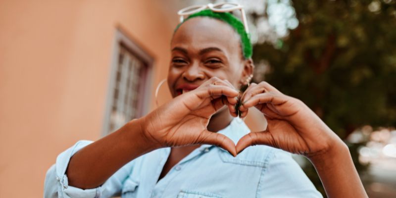 someone smiling and making a heart symbol with their hands