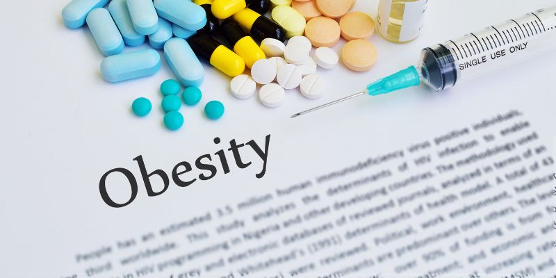 A document on Obesity with pills and a syrynge on top of it.