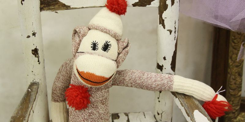 A sock monkey sitting in a wooden chair.