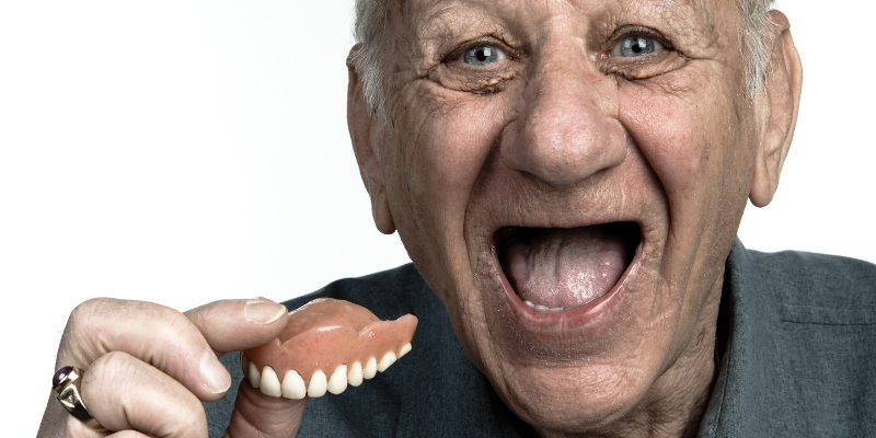 A cute old person holding their denture in their hand