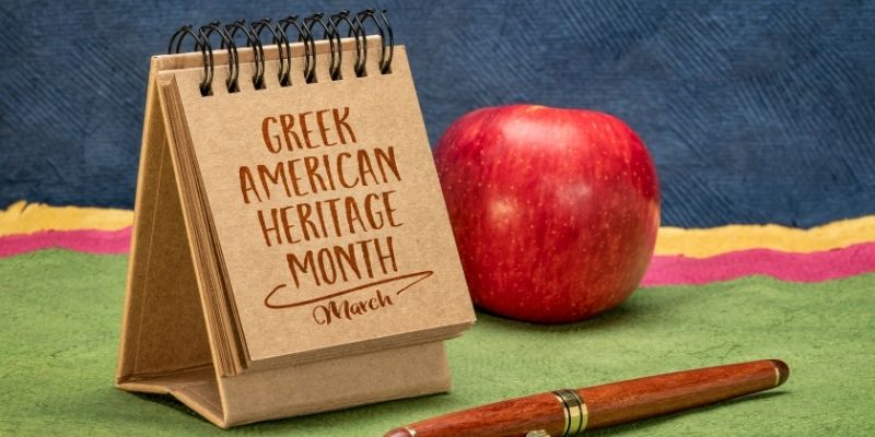 An apple next to a notepad with "Greek American Heritage Month" on the cover