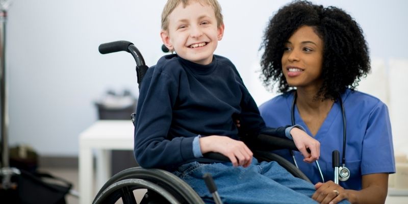 An adorable child in a wheelchair with a nurse next to him at his eye level.