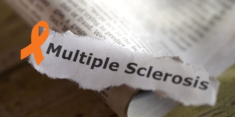 Orange ribbon next to a torn paper with multiple sclerosis written on it.