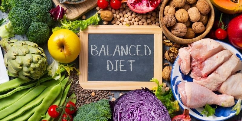 A mini chalk board with "Balanced Diet" written on it surrounded by foods in each of the major food groups.