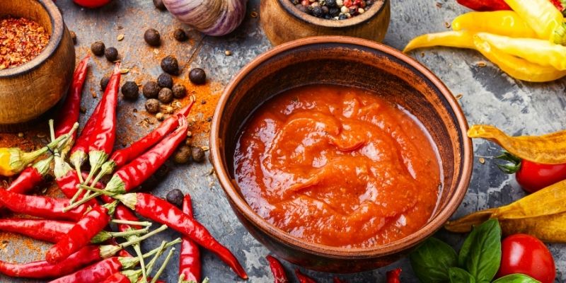 A bowl of tomato-based souce covered with peppers